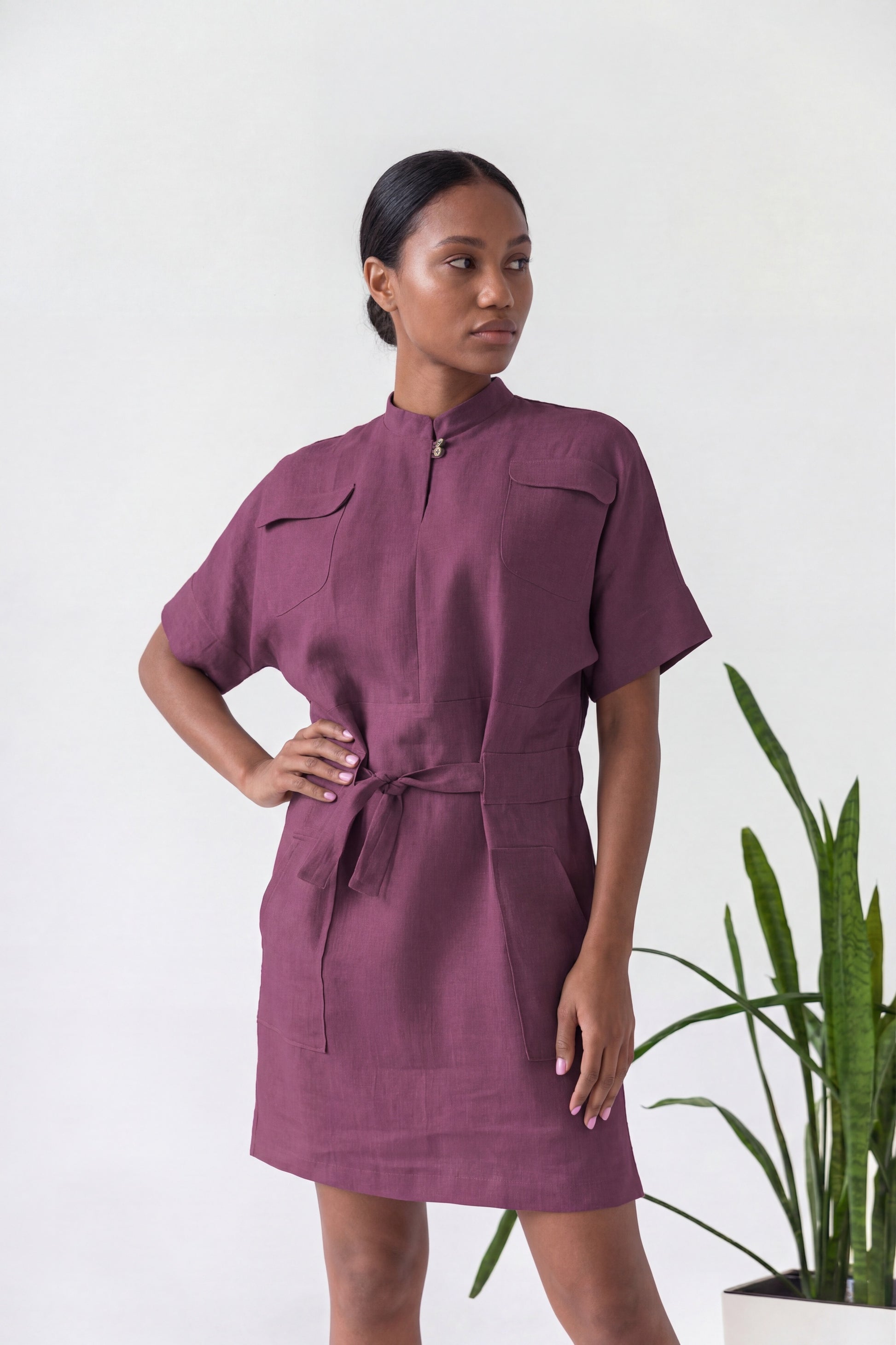 Woman wearing a purple dress standing next to a plant on a white background